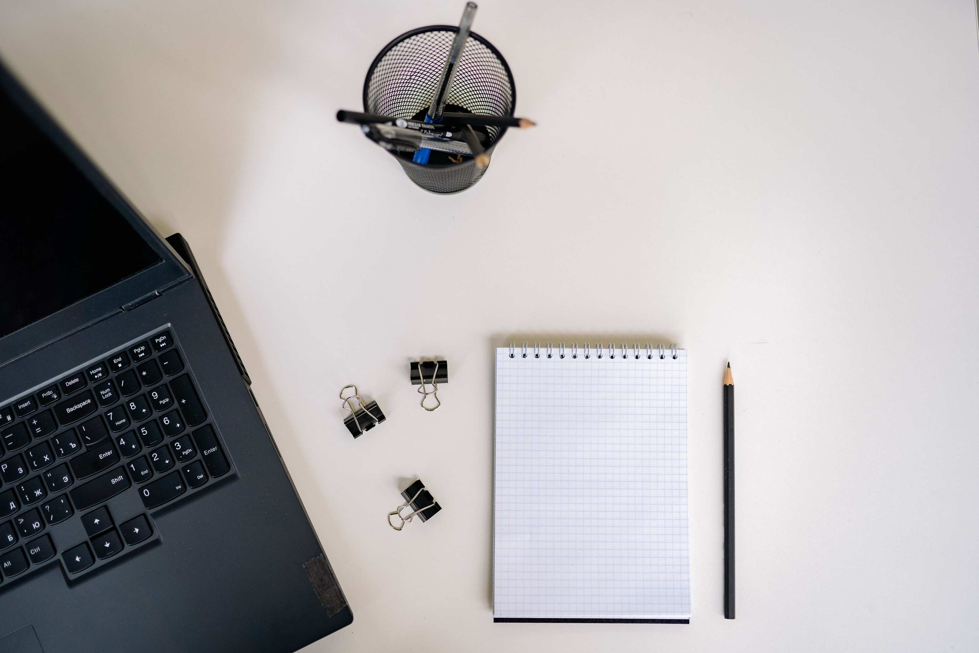 Office workspace seen from above with a laptop, notepad, and pencils on a white desk